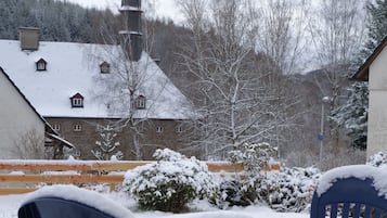 A snow-covered outdoor seating area with a view of a building with multiple windows and a chimney.