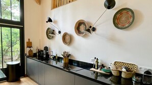 Una cocina moderna con encimera negra, armarios de madera y un ventanal grande. Se observan platos decorativos en la pared y diversos utensilios de cocina sobre la encimera.