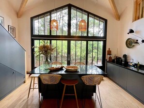 A modern kitchen with a large window, wooden ceiling beams, and a dining area with a glass table and wicker chairs. - Modern Villa with Cap Ferret feeling A0306 (Lège-Cap-Ferret)