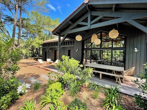A wooden deck with outdoor seating, surrounded by a garden with various plants and a clear sky.
