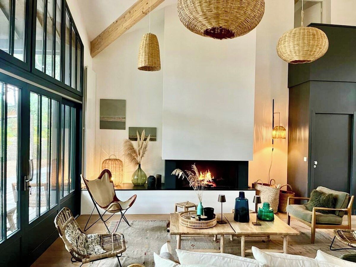 A modern living room with a fireplace, large windows, and wicker furniture.