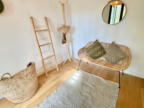 Habitació amb un petó de fibra, una escala, una cistella de fibra, una cadira de fibra i un mirall rodó a la paret.
