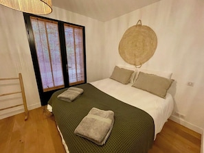 A bedroom with a bed, pillows, a woven wall hanging, a wooden chair, and a window with blinds.
