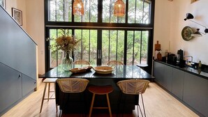 Una cocina moderna con un amplio ventanal, vigas de techo de madera y un comedor con mesa de vidrio y sillas de mimbre.