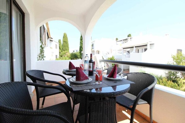 A balcony with a table set for two, featuring black wicker chairs and red napkins.