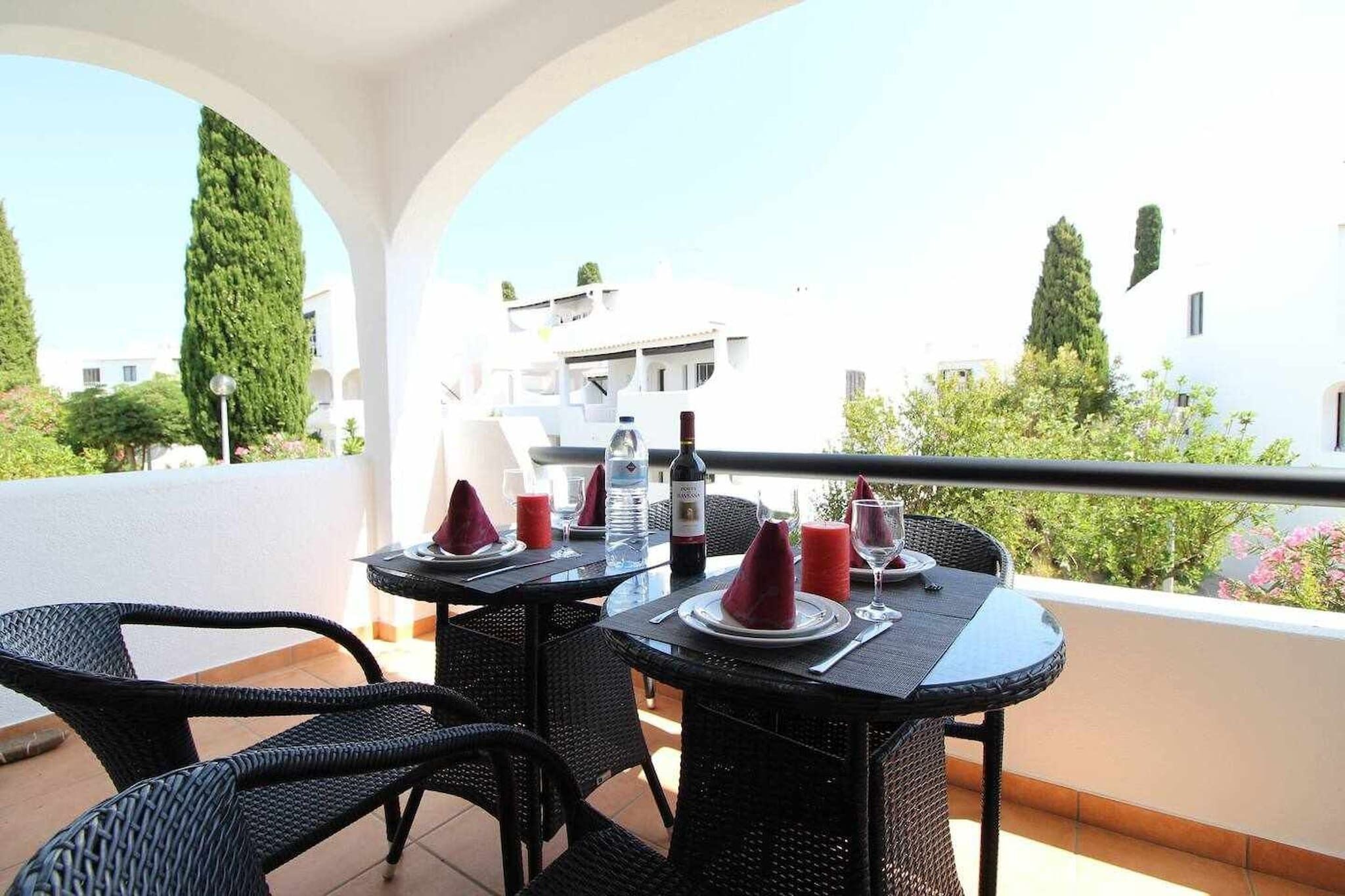 Ein Balkon mit Esstisch, ausgestattet mit einer Weinflasche, Gläsern und roten Servietten.