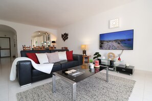 A modern living room with a black leather sofa, a glass coffee table, and a flat-screen TV mounted on the wall. - 2 Bedroom Apartment with Swimming pool at São Rafael Beach - Albufeira (Albufeira)