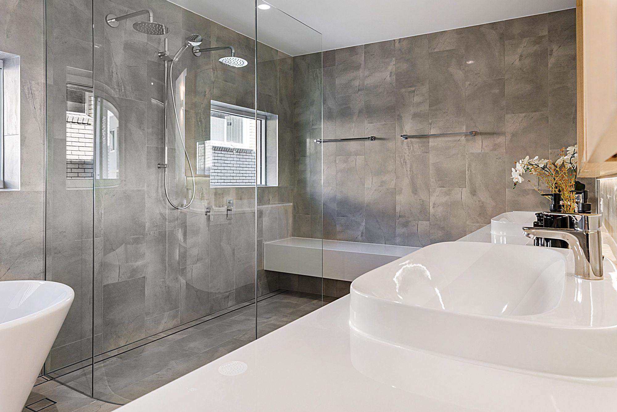 Un baño moderno con ducha envuelta en vidrio, una bañera blanca amplia y una ventana.