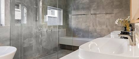 Un baño moderno con ducha envuelta en vidrio, una bañera blanca amplia y una ventana.