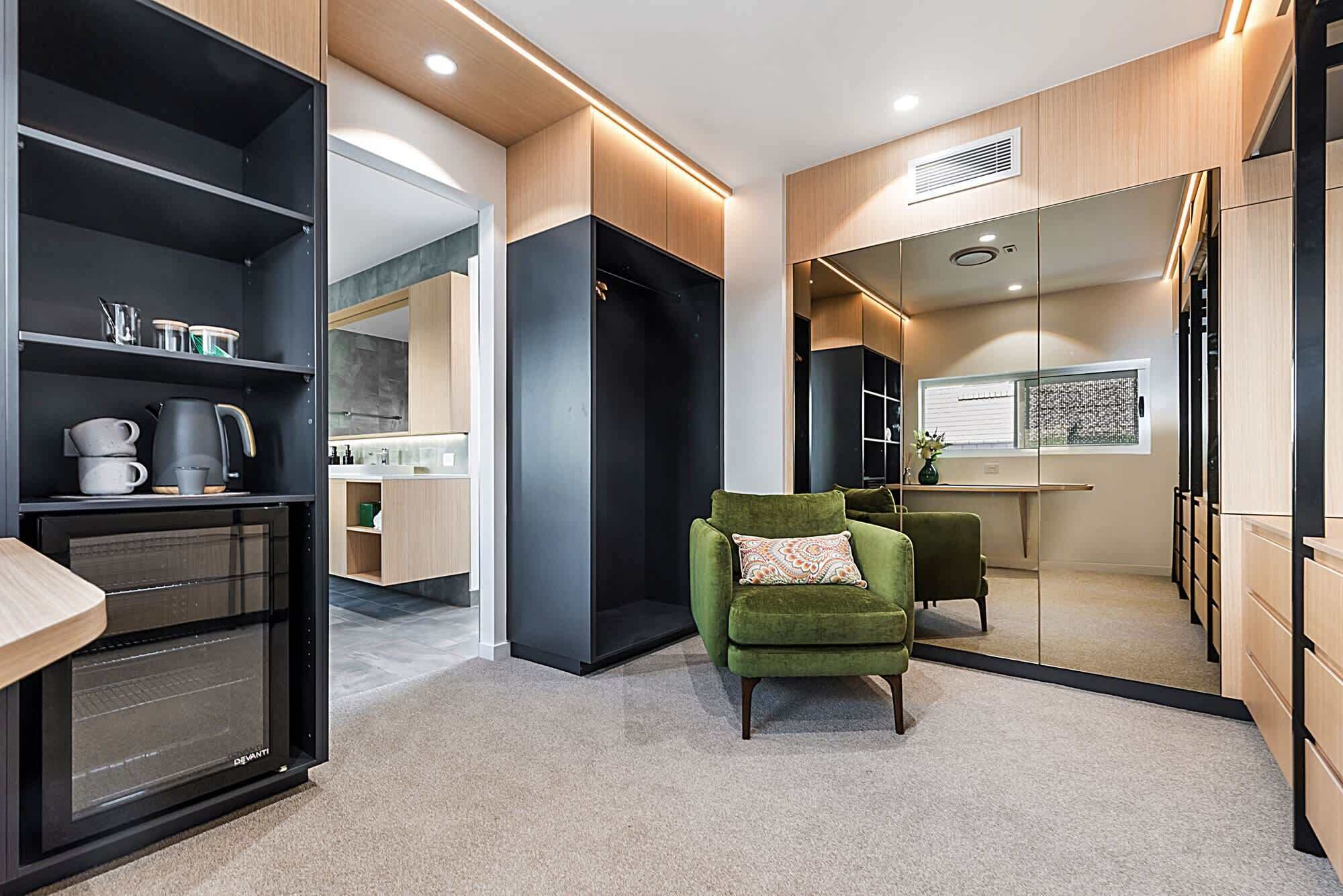 Une cuisine moderne dotée d’un four encastré, d’un fauteuil vert et d’un grand miroir.