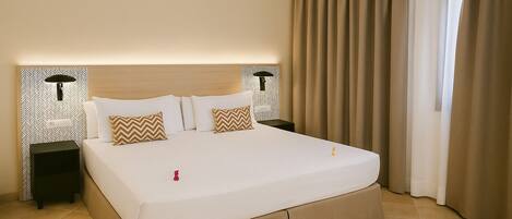 Una habitación de hotel con una cama grande, dos mesitas de noche, una lámpara de pared y una ventana con cortinas.
