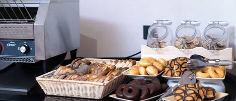 A breakfast buffet with various breads, pastries, and donuts.