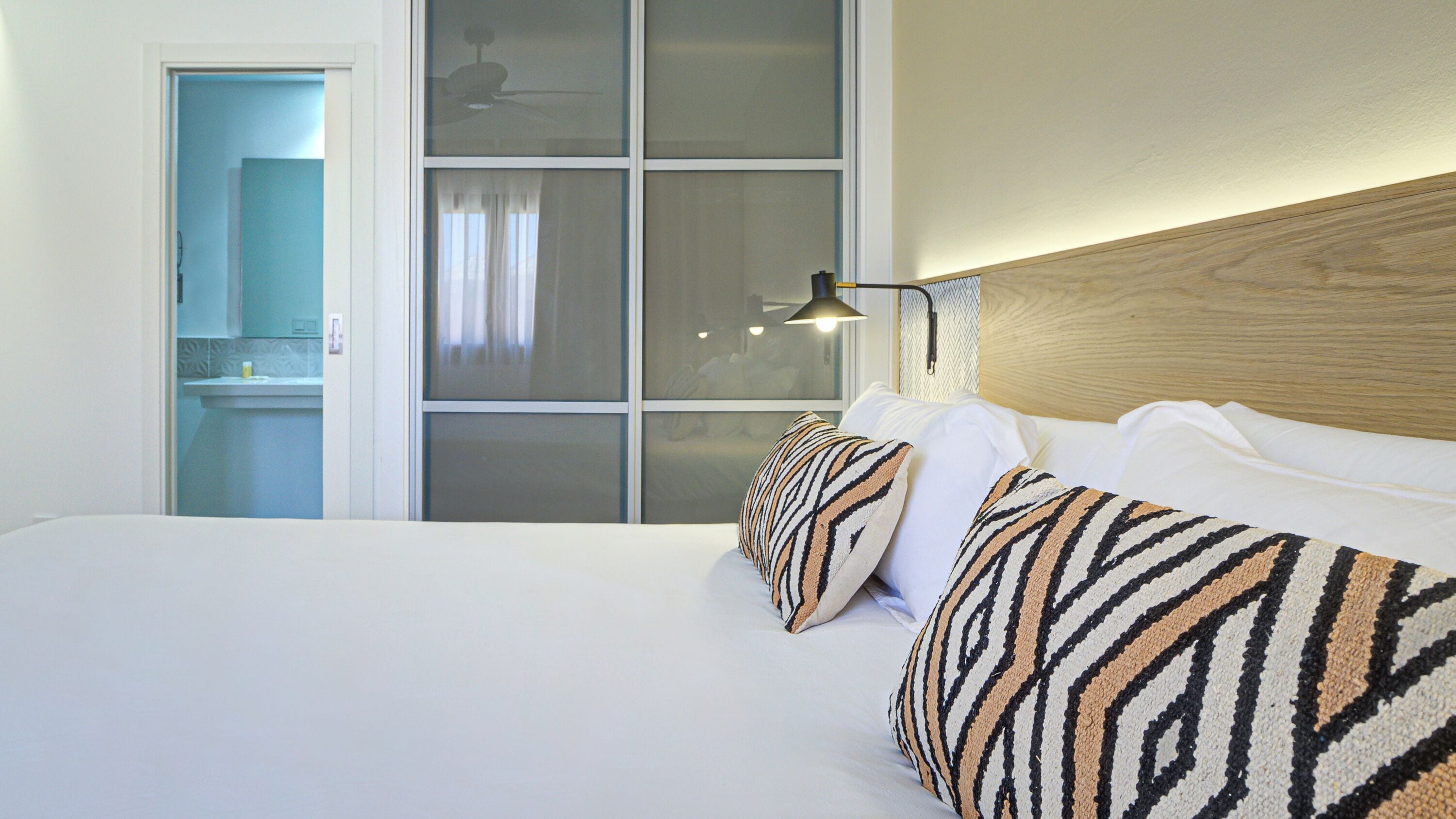 A hotel room with a large bed, a nightstand, a window with curtains, and a bathroom visible through an open door.
