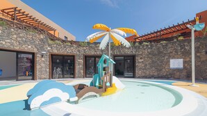 Zwembadgedeelte met een waterglijbaan, een palmboomsculptuur en een stenen muur.