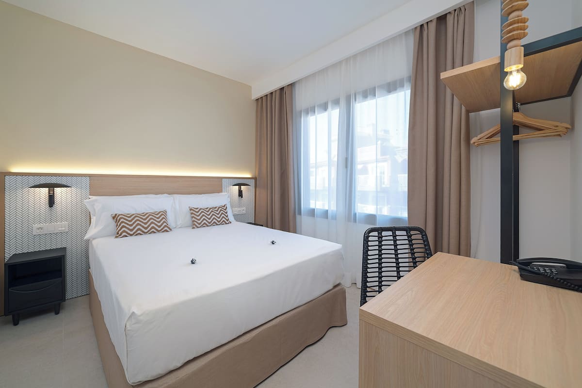 A hotel room with a large bed, bedside tables, a desk, and a chair.