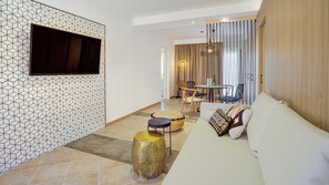 Un soggiorno moderno con una parete a motivi geometrici, un televisore a schermo piatto, un divano con cuscini decorati e un'area pranzo con sedie e tavolo.