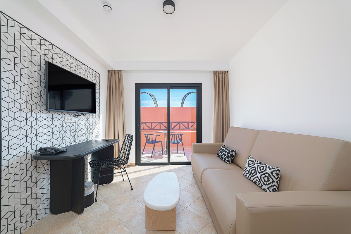 Una sala de estar moderna con una televisión de pantalla plana, un escritorio, un sofá y un balcón con vistas.