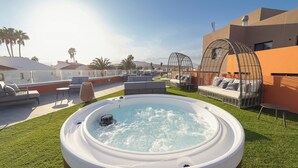 Een dakterras met een zwembad, een jacuzzi, buitenmeubilair en uitzicht op palmbomen en bergen.