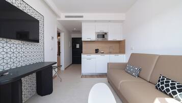 Een moderne keuken met witte kasten, een magnetron en een koffiezetapparaat. Er is een beige bank met gestreepte kussens en een witte voetenbank.