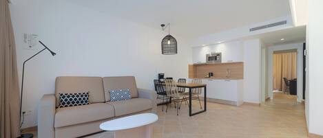 A modern living room with a sofa, coffee table, dining table, and chairs. There is a kitchen area with a microwave and cabinets.