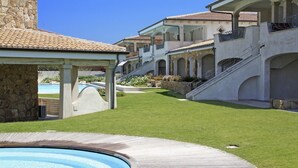 Un espace piscine doté d’une terrasse en bois, d’un mur en pierre et d’un bâtiment avec un toit en tuiles et des arcades.