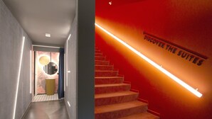 Un intérieur d’hôtel moderne avec un escalier menant aux suites, un couloir éclairé par un luminaire et un mur sur lequel est affiché un panneau indiquant : « DÉCOUVREZ LES SUITES ».