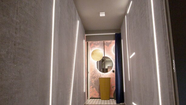 Un couloir au design moderne, doté d’un sol carrelé et de murs ornés de bandes lumineuses verticales.