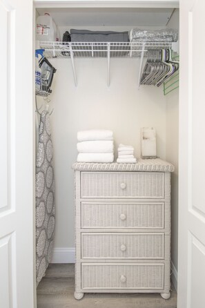 A white wicker dresser with drawers, a white shelf above, and a shower curtain with a leaf pattern.