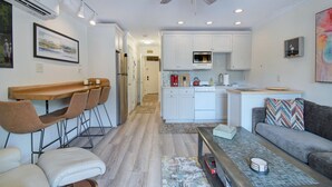 A modern kitchen with white cabinets, a microwave, and a coffee maker. There is a dining area with a wooden table and chairs.
