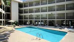 A multi-story hotel with a swimming pool, outdoor seating, and a palm tree.