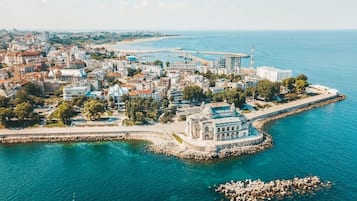 An aerial view of a coastal city with a prominent historical building, a marina, and a rocky breakwater.
