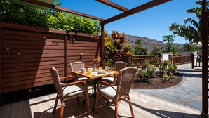 Un patio al aire libre con una mesa de madera y sillas de mimbre, rodeado por una valla de madera y plantas en macetas.