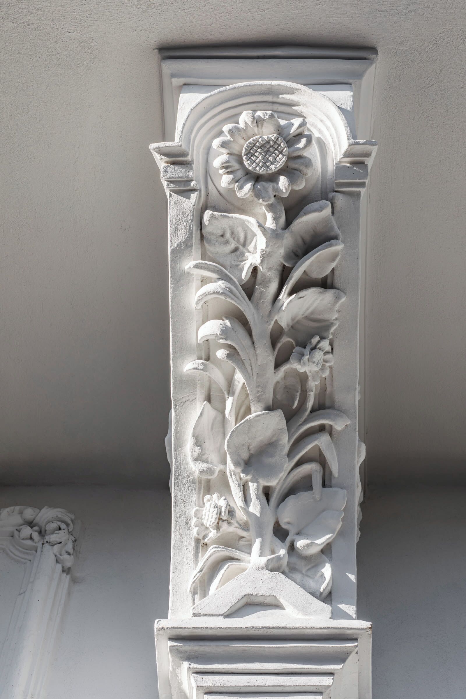 Un élément architectural blanc orné d’un motif floral comprenant des feuilles et une fleur.