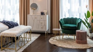Un salon moderne avec un lustre, un fauteuil vert, un meuble blanc et un miroir rond.