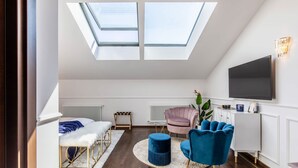 Une chambre de style loft moderne, dotée de fenêtres de toit, d’un lit, d’un coin salon avec un fauteuil bleu et d’un téléviseur fixé au mur.