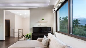 A modern living room with a beige sofa, a flat-screen TV, a small plant, and a window with a view of palm trees. - Villa Elisabeth View luxurious with POOL & BBQ !!! (CHANIA GREECE)