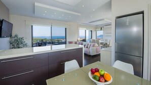 A modern kitchen with a large island, a dining area with a fruit bowl, and a view of the sea. - Villa Elisabeth View luxurious with POOL & BBQ !!! (CHANIA GREECE)