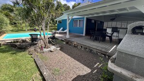 En baghave med swimmingpool, udendørs møbler og en overdækket terrasse.