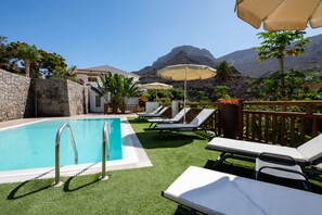 Relax by the serene pool surrounded by lush greenery and a mountain backdrop.