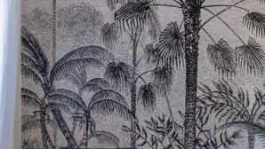Een slaapkamer met een bed, kussens en een muur met een tropische plantenmuur.