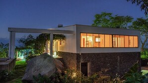 Une maison moderne avec une façade en pierre, de grandes fenêtres et une pergola illuminée.