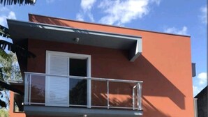 Un edificio moderno de dos pisos con fachada roja, un balcón y una escalera que conduce a la entrada.