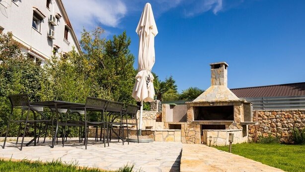 An outdoor patio with a stone table and chairs, a covered umbrella, and a stone fireplace.