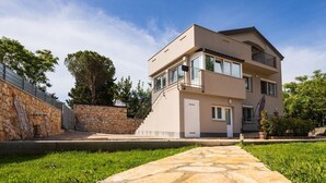 A modern two-story house with a stone facade, a balcony, and a stone pathway leading to the entrance.