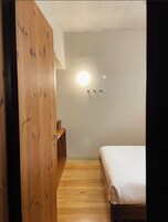 Un dormitorio con un armario de madera, una cama y una lámpara fijada a la pared.