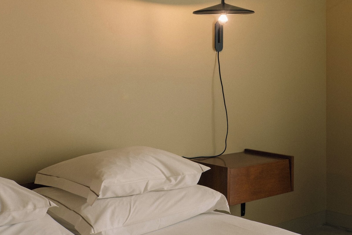 Ein Hotelzimmer mit Bett, Kissen, Nachttisch und Wandlampe.