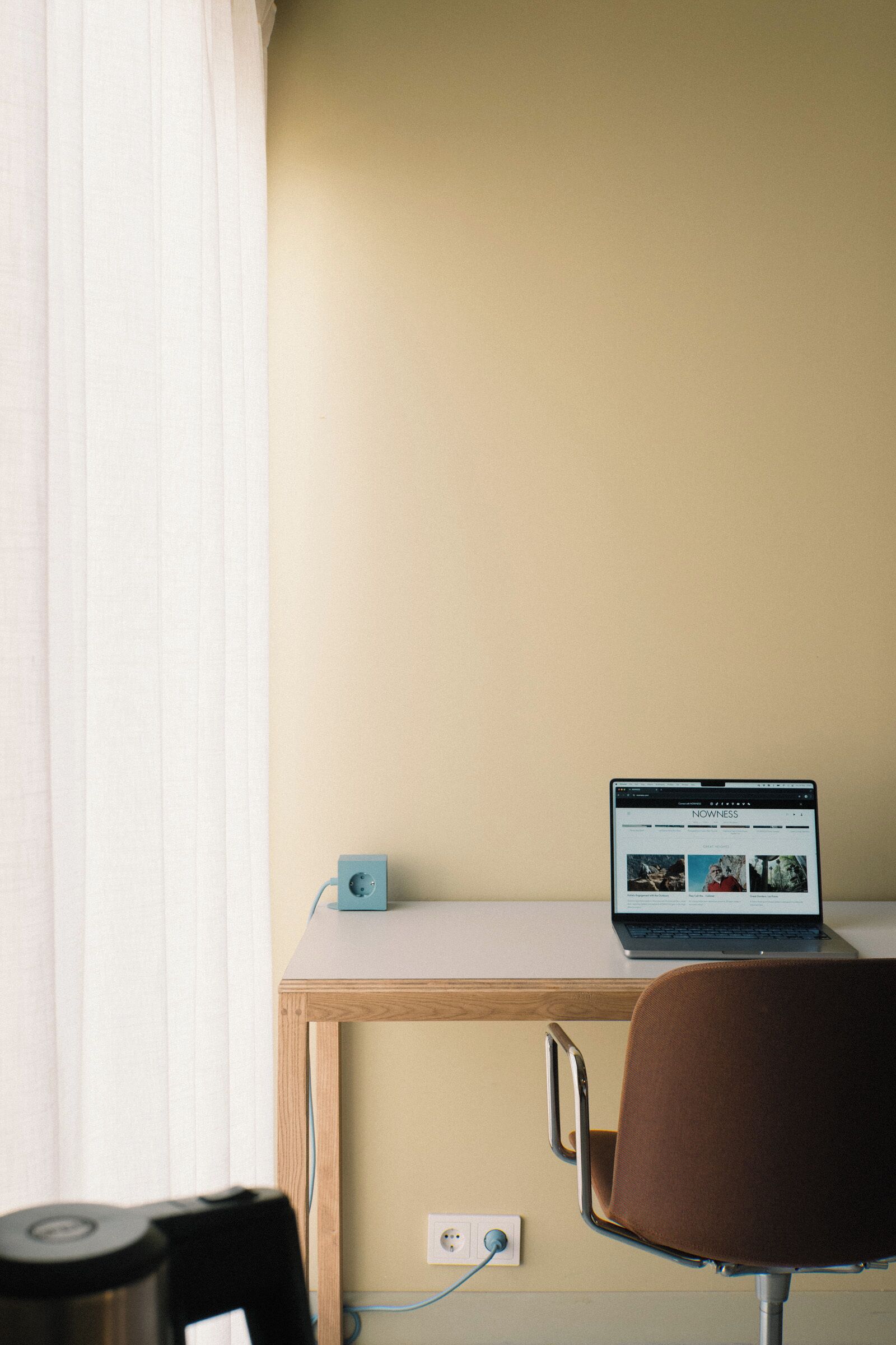 A laptop on a wooden desk with a power outlet and a cable.
