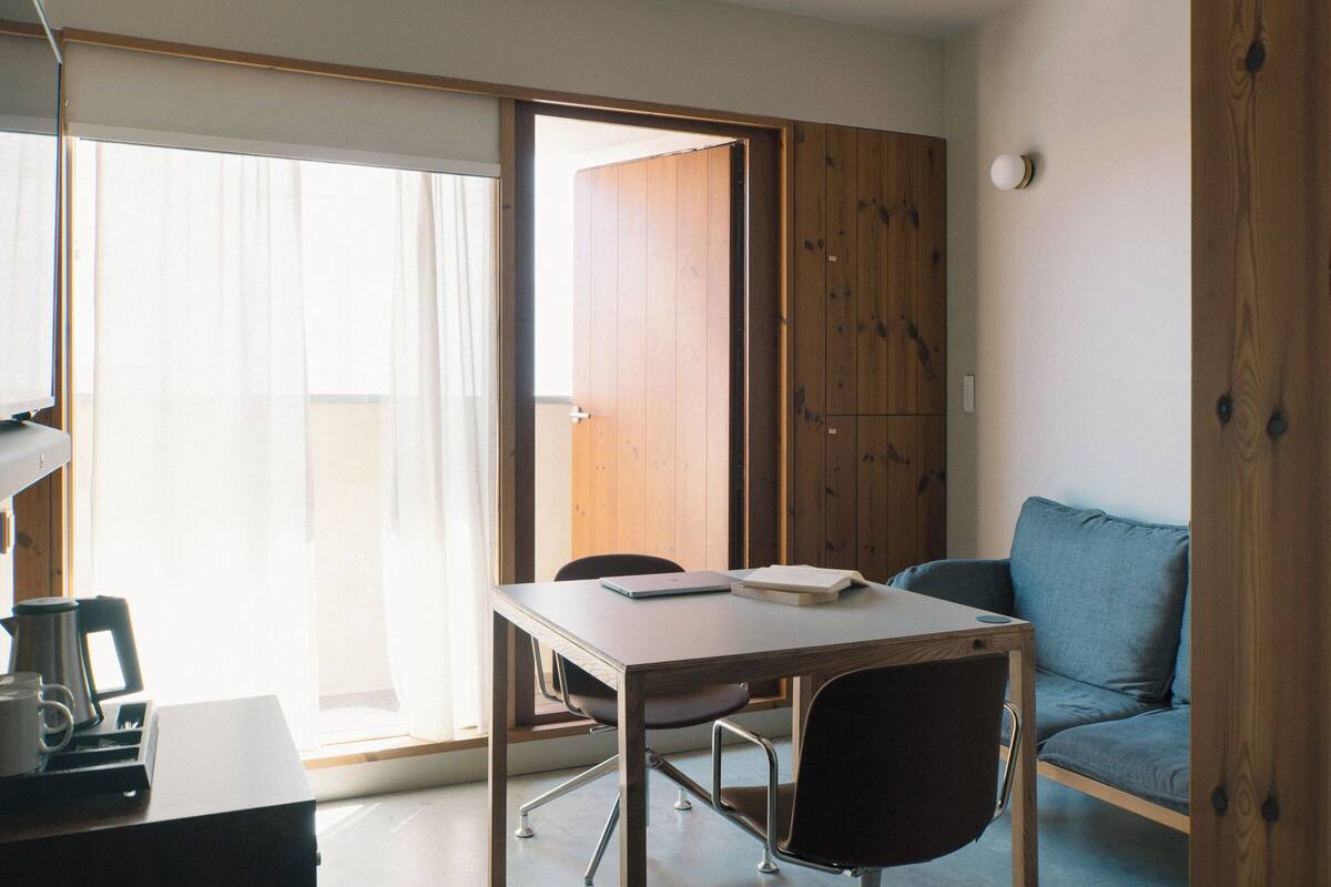 Ein Zimmer mit Holztür, einem Tisch mit Stühlen, einem blauen Sofa und einer Kaffeemaschine.