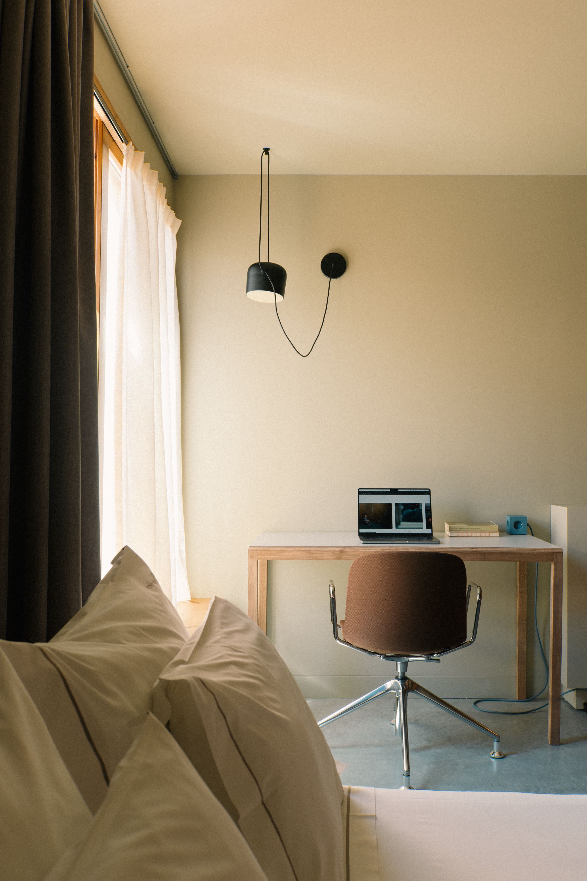 Une chambre d’hôtel avec un lit, un bureau avec un ordinateur portable, une chaise et une lampe fixée au mur.