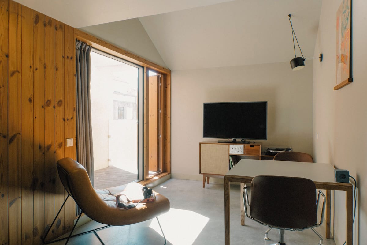 Ein modernes Wohnzimmer mit einer Holzwand, einem Fernseher, einem Esstisch und einem Sessel.